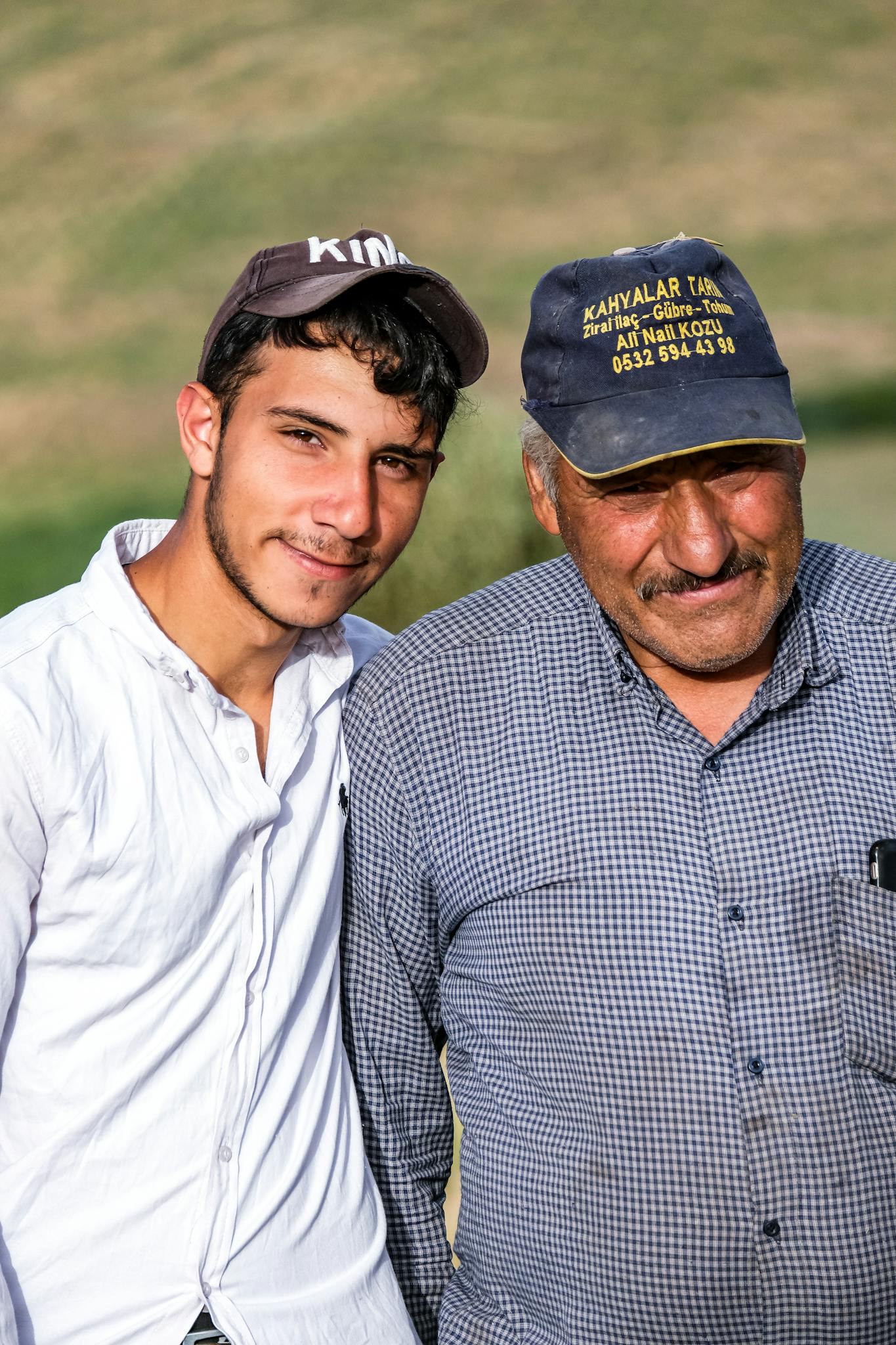 Portrait of a smiling father and son in casual attire outdoors in sunlight.